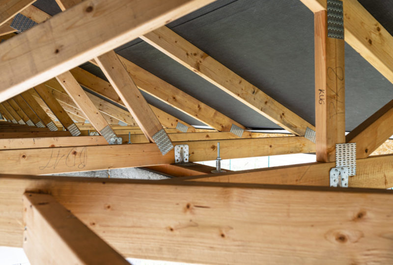 Roof trusses covered with a membrane on a detached house under construction, view from the inside, visible roof elements and truss plates.